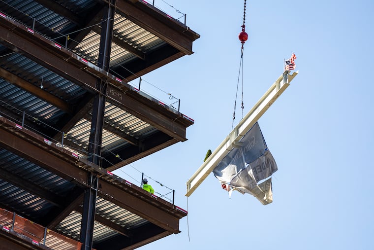 A large white metal beam with signatures from community members, workers, and organizations is raised to the top of a building and added to the construction in the Schuylkill Yards project in Philadelphia.