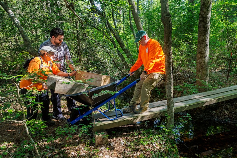 Ro Mason (from left), volunteer Drew Brickner, and Frank Carr muscle a load of wood along a wooded bridge. The wood will be used by the members and volunteers with Outdoor Club of South Jersey to repair hiking trails near Batsto Village in Hammonton, N.J.
